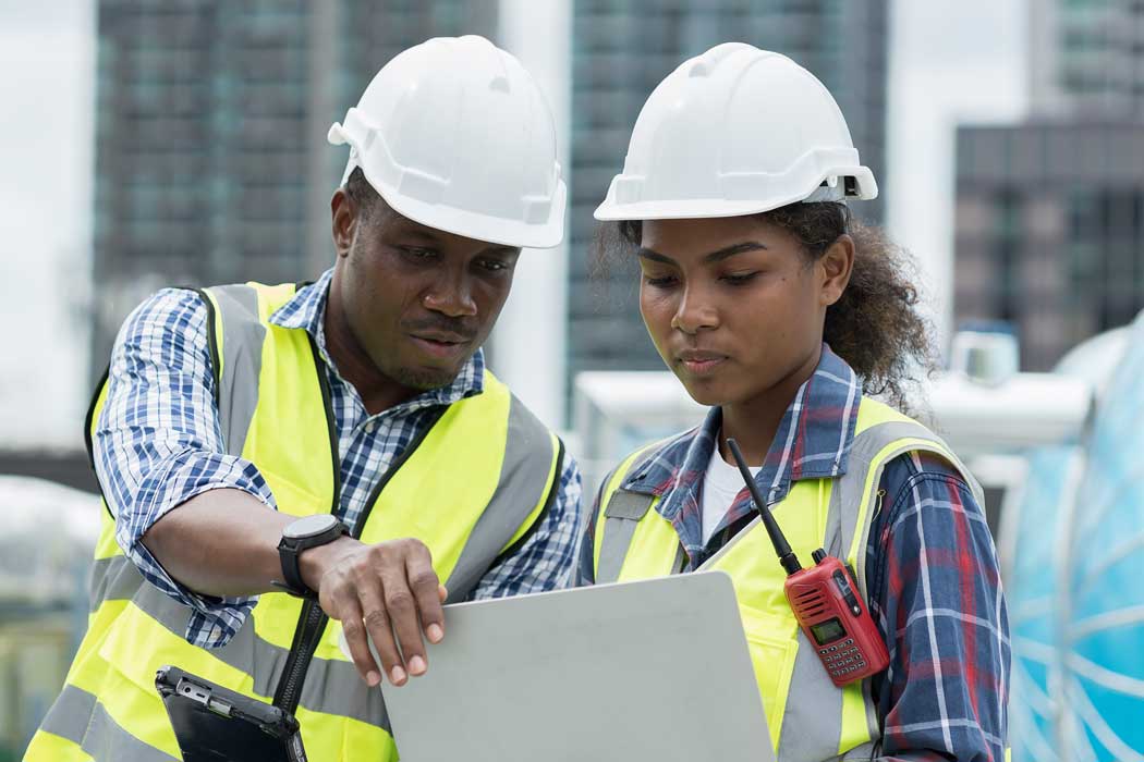 Two workers on a construction site looking at a laptop